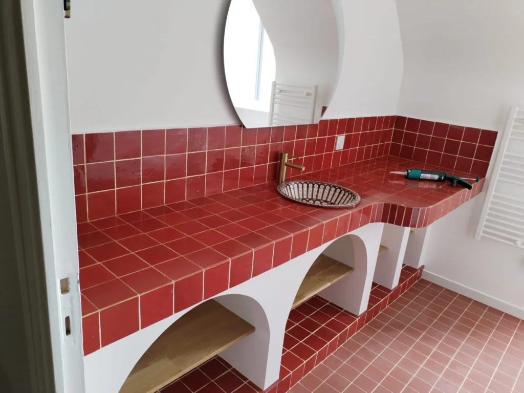 Plan de travail de salle de bain en carrelage rouge avec vasque décorative, robinetterie dorée et niches arrondies intégrées