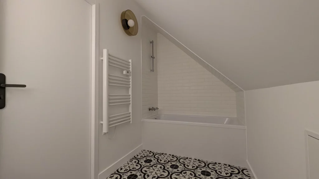 Salle de bain rénovée noir et blanc avec baignoire et miroir rétro éclairé dans un aménagement de combles à Orgères (35)
