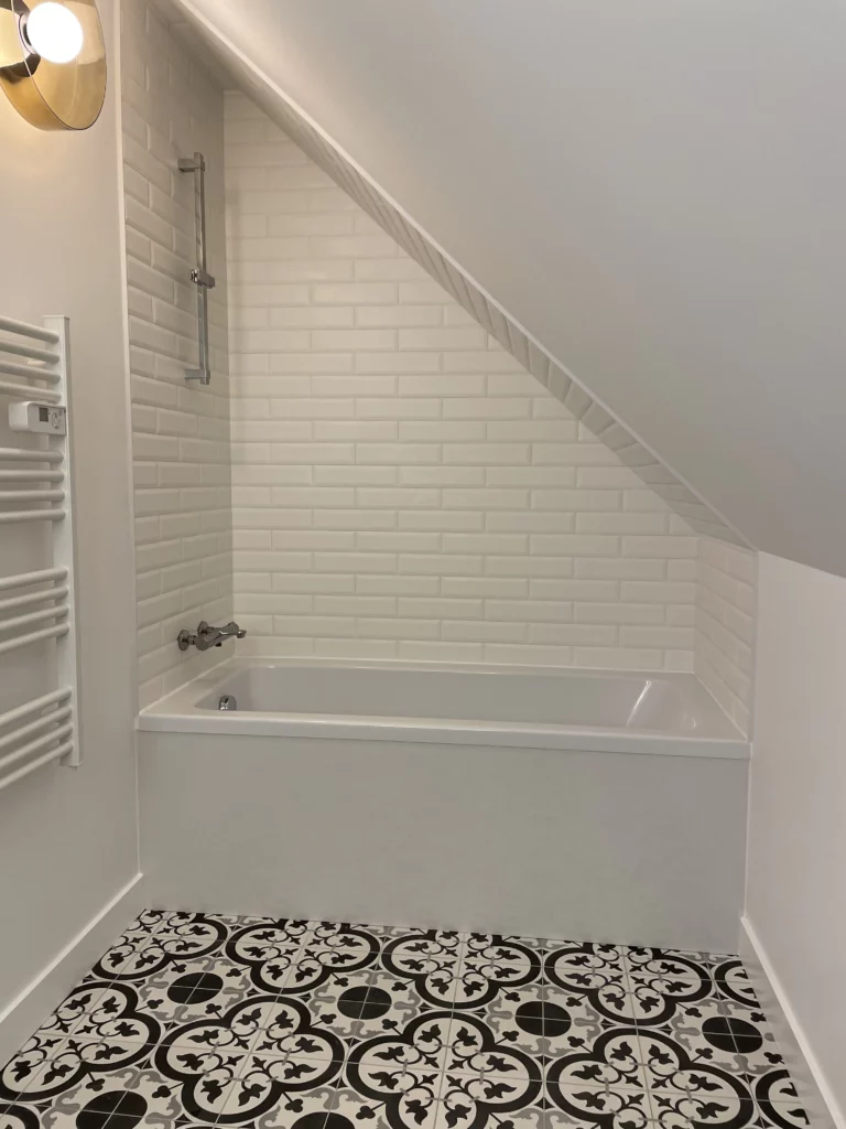 Salle de bain rénovée noir et blanc avec baignoire et miroir rétro éclairé dans un aménagement de combles à Orgères (35)