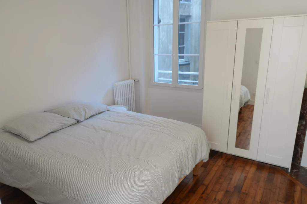 Chambre rénovée en location avec lit double, bureau de travail et espace de rangement.