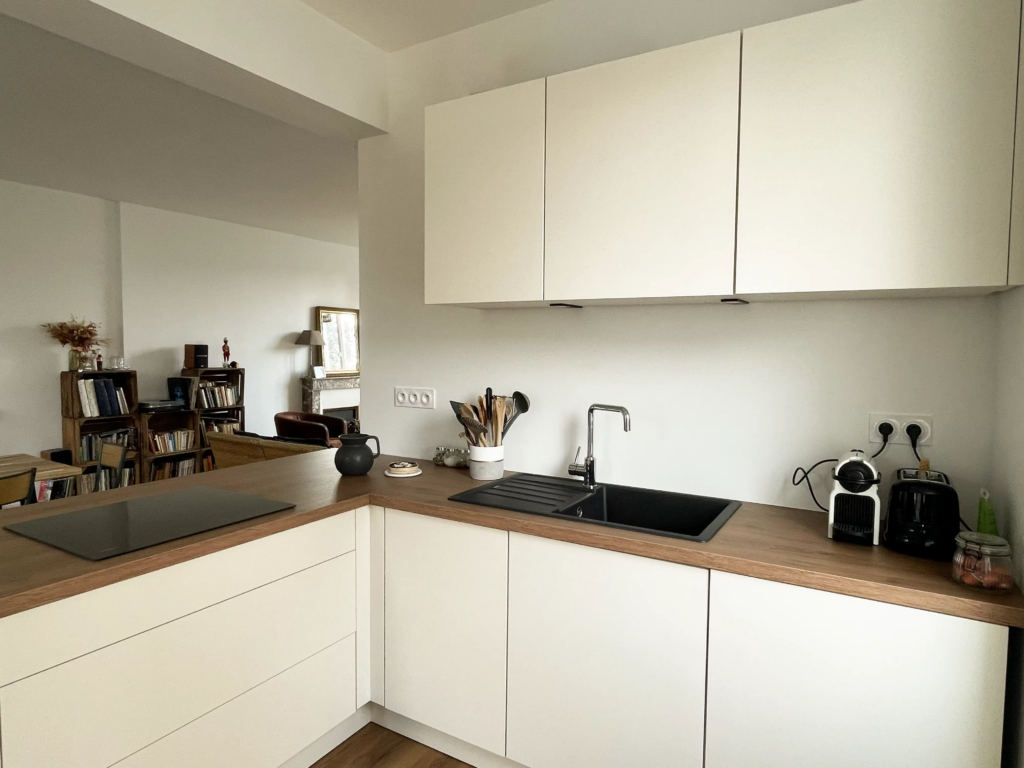 Cuisine rénovée vue de face avec évier noir, nouveaux aménagements et rénovation du salon attenant