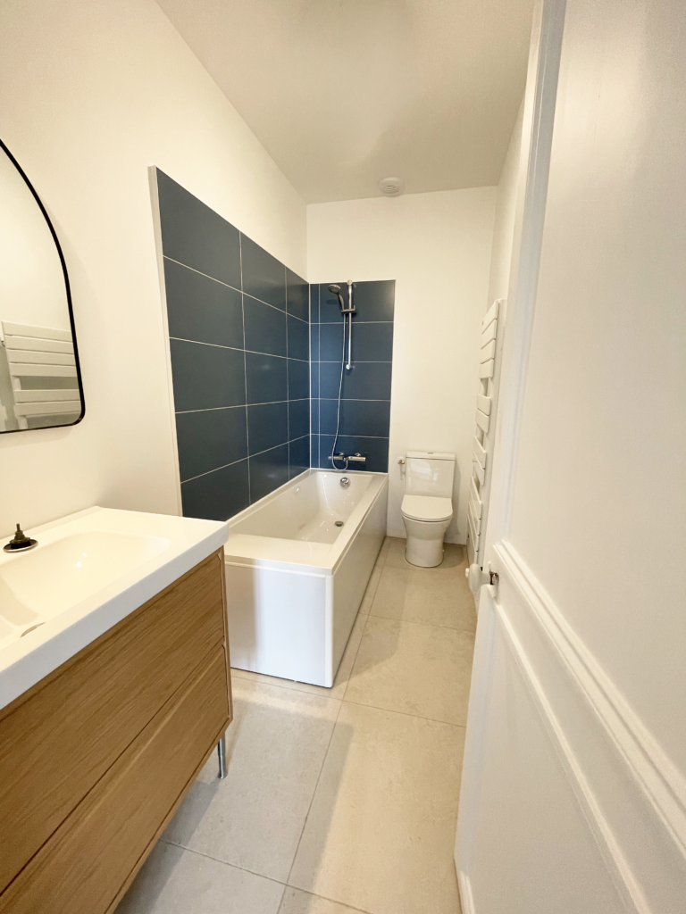 Salle de bain rénovée avec carrelage bleu, meuble vasque en bois et aménagement intérieur moderne